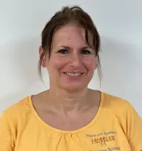 Lächelnde Frau mit braunen Haaren, die ein gelbes Hemd trägt und vor einem schlichten weißen Hintergrund steht.